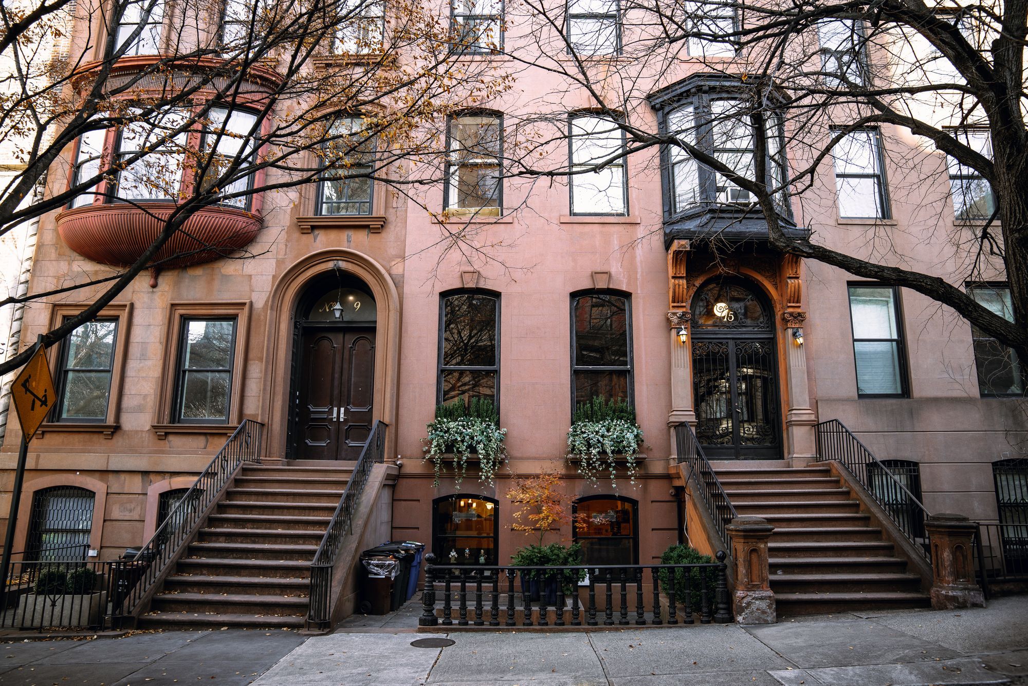 A row of brownstones with front stoops on a tree-lined street in fall