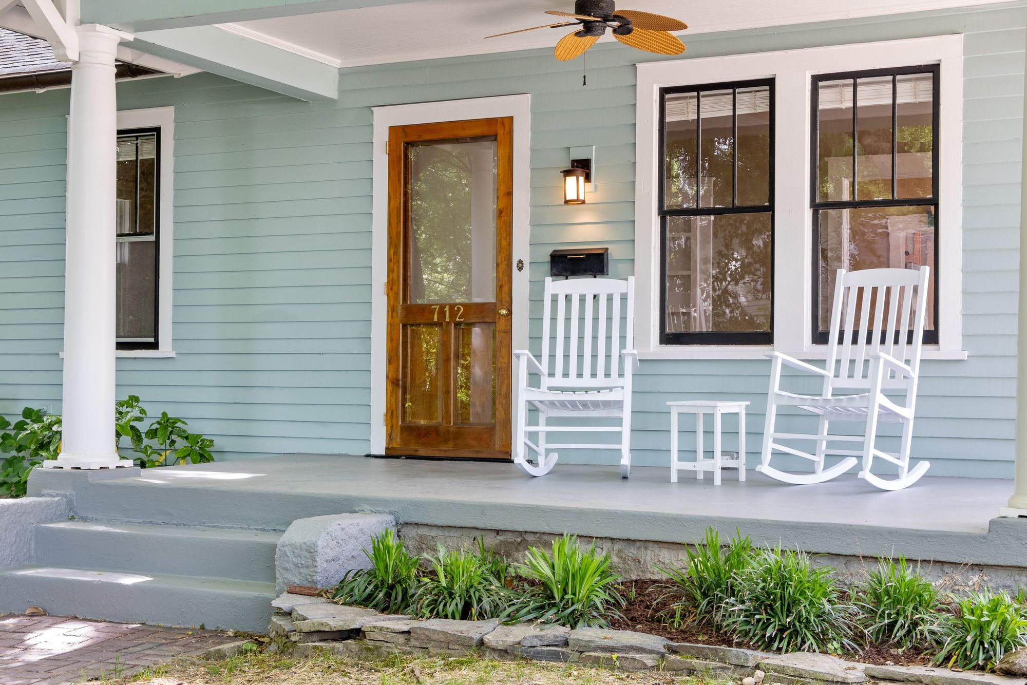 Front porch of a house with two white rocking chairs beside a wooden front door